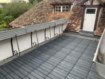 Terrasse de toit en lames composites, garde-corps en ferronnerie, porte blanche et toit de tuiles