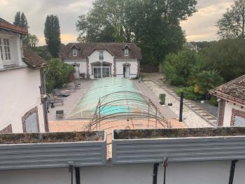 La piscine et son abri télescopique vus d'en haut, la maison et le parc autour