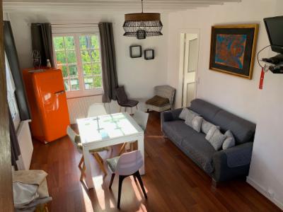 Séjour du gîte : canapé gris, réfrigérateur orange, table blanche et téléviseur