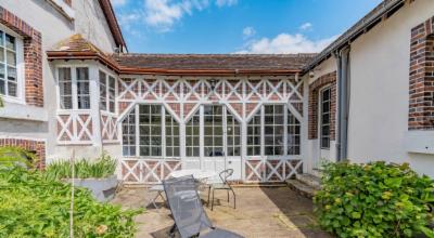 Véranda à colombages blancs et rouges ouvrant sur une terrasse, transats installés devant