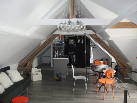 Loft sous charpente en A, canapé noir, table de repas et chaises orange